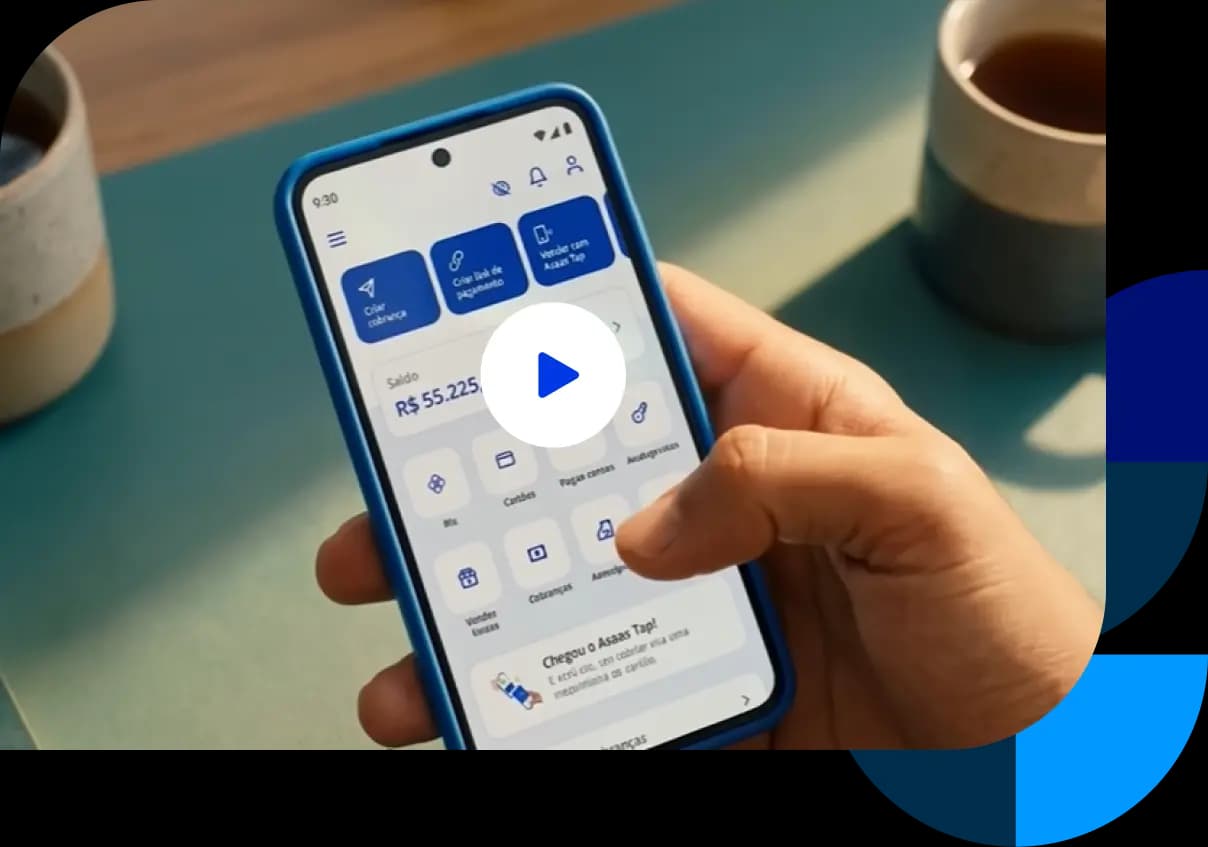 Pessoa segurando um smartphone exibindo o aplicativo do Asaas na tela, mostrando saldo e opções financeiras, enquanto está sentada à mesa com xícaras ao fundo